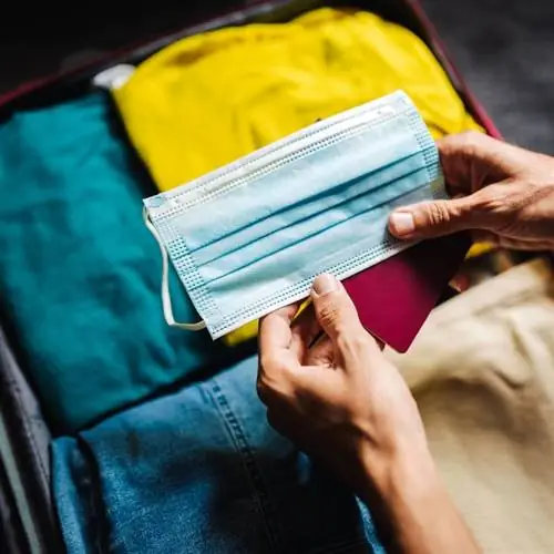 Путешественник держит маску в руках, пакуя багаж перед международным путешествием
