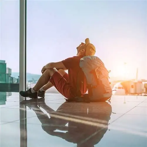 Турист, прислонив голову к собственному рюкзаку, сидя на полу аэропорта