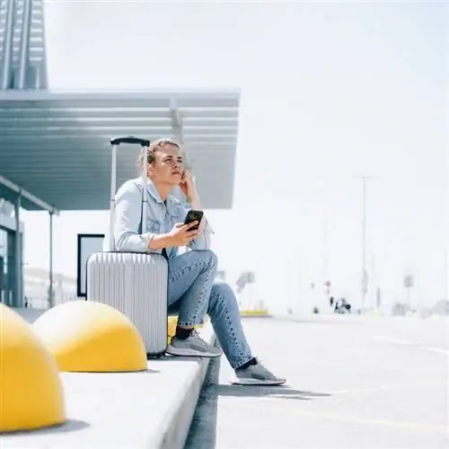 Молодая женщина-путешественница выглядит расстроенной, сидя на обочине в международном аэропорту или на вокзале в пункте посадки и высадки