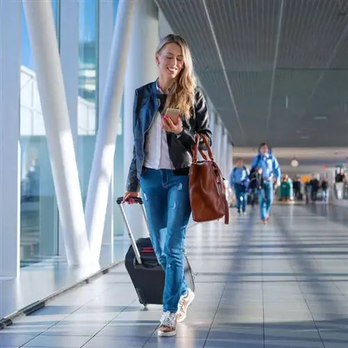 Счастливая молодая женщина проверяет свой телефон по пути к выходу на посадку в международном аэропорту