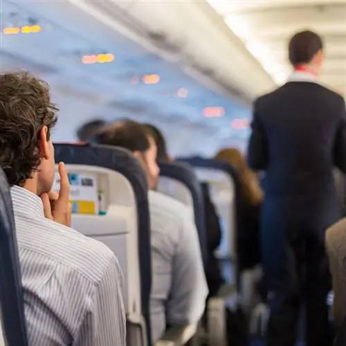 Пассажиры на фото внутри самолета, когда экипаж идет по коридору