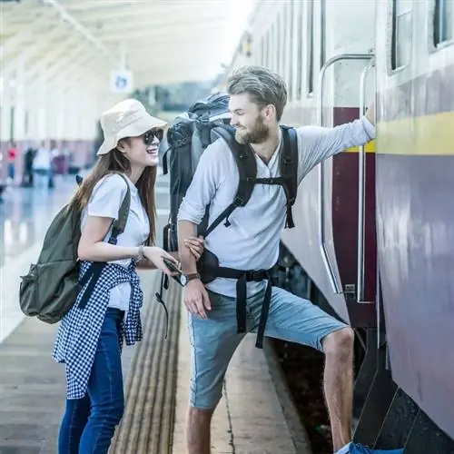 Пара молодых счастливых путешественников, садящихся в поезд, концепция путешествия на поезде