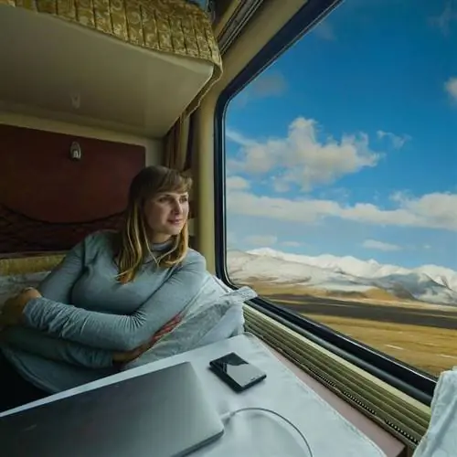 Улыбающаяся путешественница, совершающая живописное путешествие на поезде по заснеженным горам ради вида