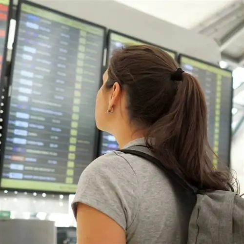 Молодая путешественница с рюкзаком внимательно наблюдает за информационным табло вылета в аэропорту