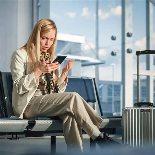 Молодая женщина-путешественница, деловая женщина, проверяющая свой телефон, хотя она выглядит шокированной или расстроенной, концепция сбоя рейса