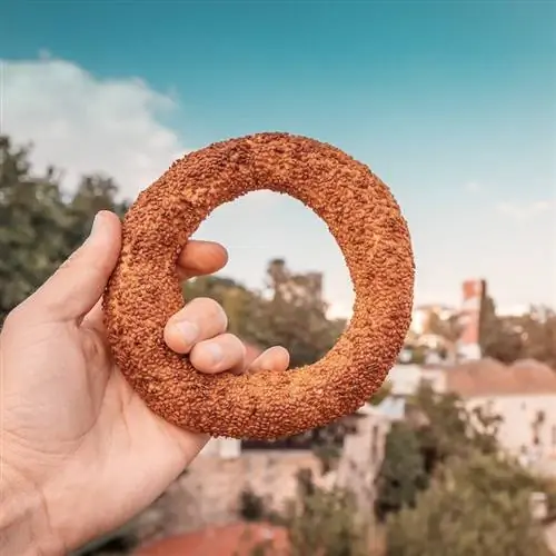 Турецкий бублик выглядит как традиционная уличная еда в руках на фоне старого города Анталии с такими знаменитыми достопримечательностями, как минарет Йивли.