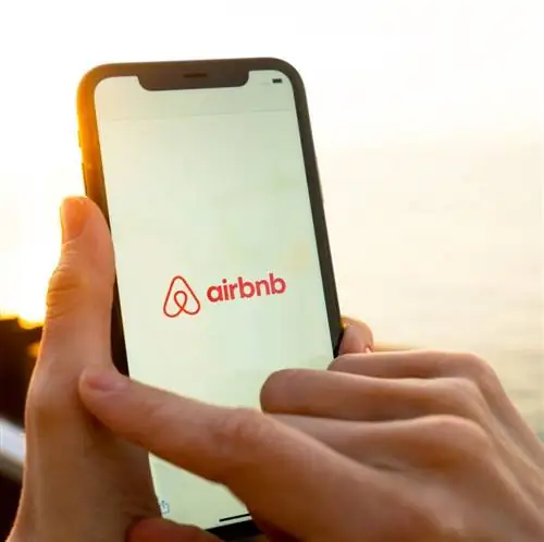 Женские руки держат смартфон с изображением Airbnb на фоне заката