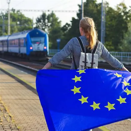 Женщина-путешественница держит флаг Евросоюза, когда поезд приближается к станции, местонахождение не указано