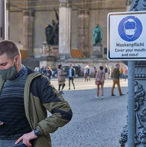 Мужчина в маске в Германии рядом с табличкой, призывающей людей носить маски