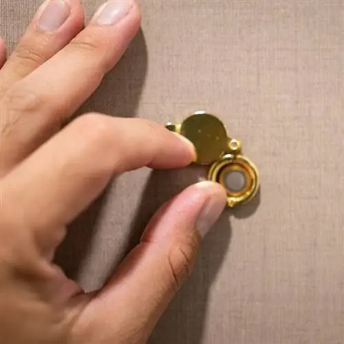 рука открывает глазок на двери комнаты. Фотография интерьера и объекта, выборочный фокус под рукой.