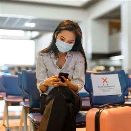 Молодая путешественница в маске во время проверки телефона в аэропорту