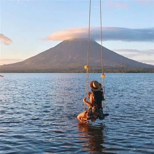 Молодая путешественница на качелях на берегу океана перед видимым вулканом в Никарагуа, Центральная Америка