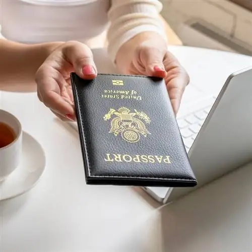 Молодая американская путешественница держит в руках футляр для паспорта США, пользуясь компьютером, концепция международного путешествия Молодая американская путешественница держит в руках футляр для паспорта США, пользуясь компьютером, концепция международного путешествия