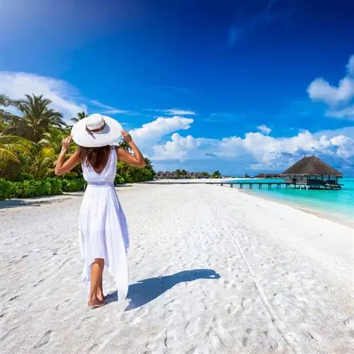 Молодая женщина в белом летнем платье бродит по тропическому карибскому пляжу