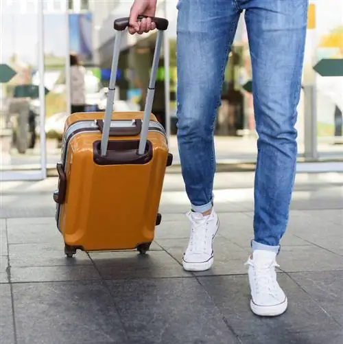 Крупным планом ноги молодого человека, идущего в аэропорт с чемоданом