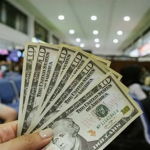 Путешественник держит доллары США в аэропорту, международные путешествия