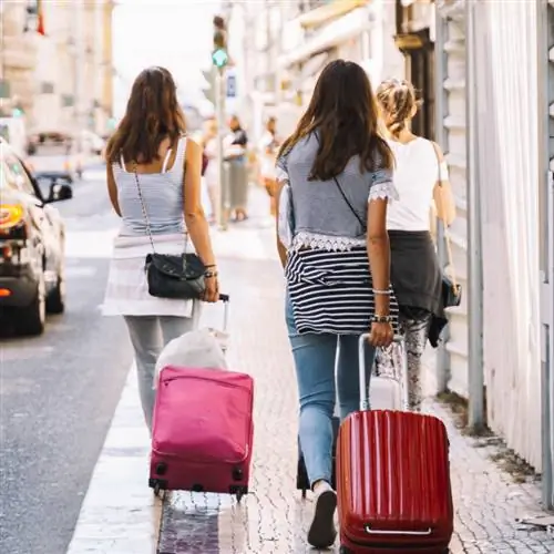 две женщины катят чемоданы по городу