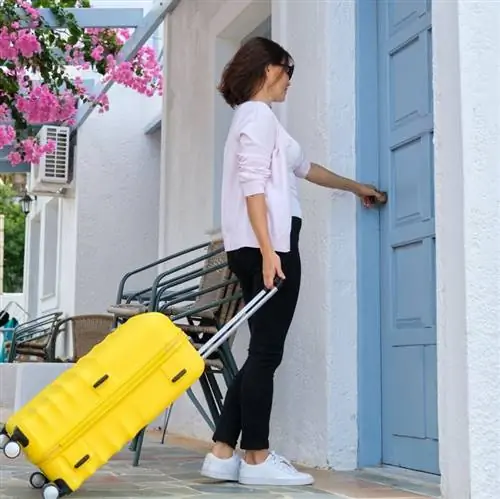 женщина тянет чемодан и открывает синюю дверь