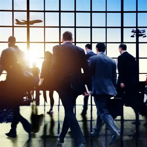 люди идут через оживленный аэропорт, и в небе виден самолет