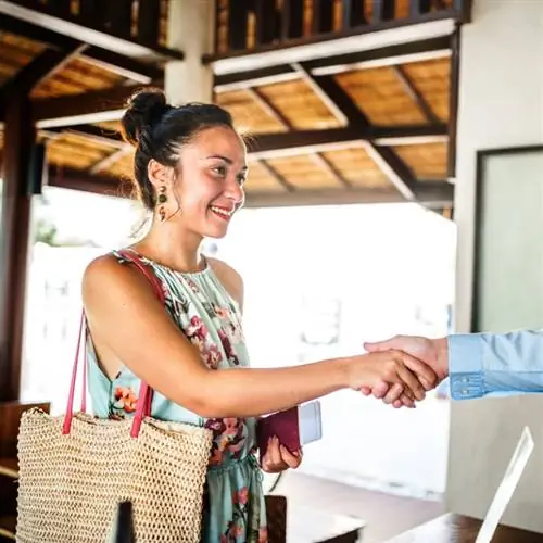 Туристка в цветочном платье пожимает руку кому-то в отеле