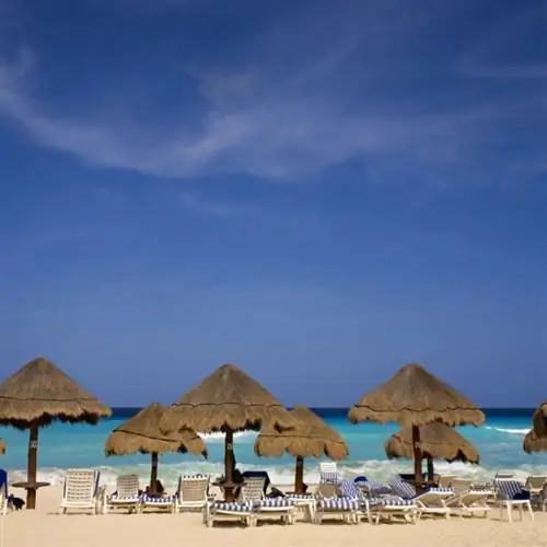 крытые соломой зонтики на мексиканском пляже, популярном среди туристов. вдали голубое небо и бирюзовые воды