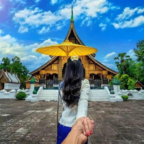 Женщина-туристка ведет своего партнера или друга за руку, пока они идут к буддийскому храму в Лаосе, Юго-Восточная Азия