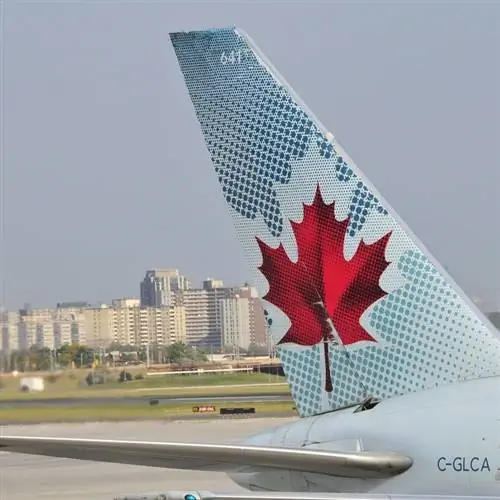 Крупным планом изображение хвоста самолета Air Canada, припаркованного в аэропорту с современными многоквартирными домами, размытыми на заднем плане, Торонто, Канада