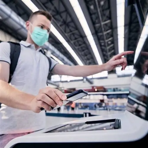 Мужчина-путешественник в маске при регистрации на рейс в аэропорту