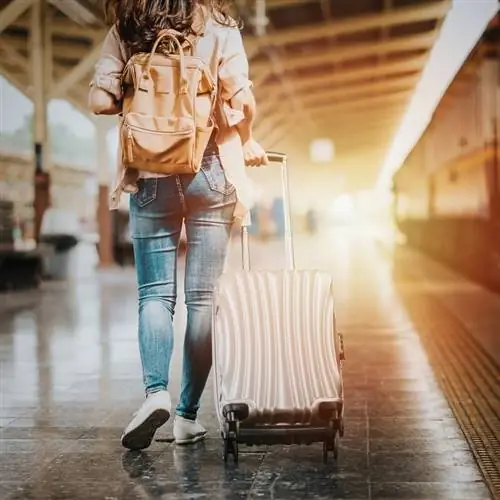 Женщина-путешественница тащит свой багаж по платформе станции перед посадкой в поезд
