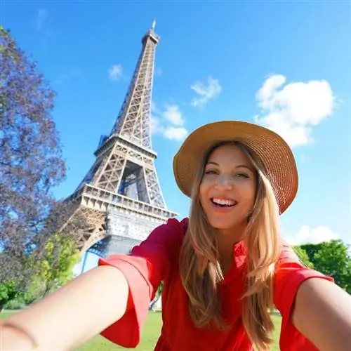 Молодая блондинка в красной летней блузке и соломенной шляпе улыбается, делая селфи с Эйфелевой башней в Париже, Франция, Европа