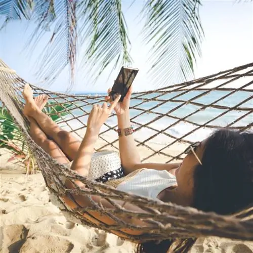 Концепция летних каникул, счастливая женщина в белом бикини, шляпе и солнцезащитных очках с помощью мобильного телефона в гамаке на тропическом пляже на закате, Ко Мак, Таиланд