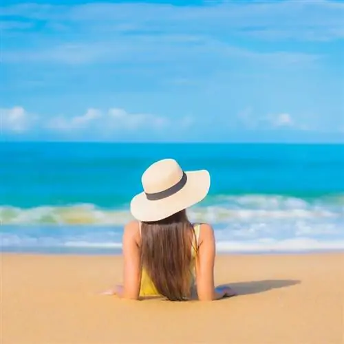 Молодая женщина в пляжном наряде и соломенной шляпе лежит на песке и смотрит на океан бирюзового цвета в тропическом месте, пляжный отдых