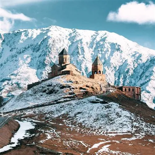 Православная церковь Гергети на фоне заснеженных вершин Степанцминды, альпийского города в Грузии, расположенного на Кавказе, в регионе между Восточной Европой и Западной Азией