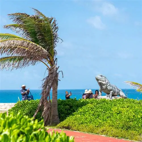 Туристы фотографируют статую игуаны в тропической обстановке с видом на Карибское море в Исла-Мухерес, Мексиканский Карибский бассейн, Мексика