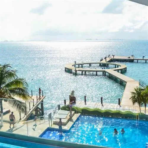 Гости курорта расслабляются в бассейне с видом на красивый пирс, уходящий в Карибское море, на острове Мухерес, Мексиканские Карибы, Мексика