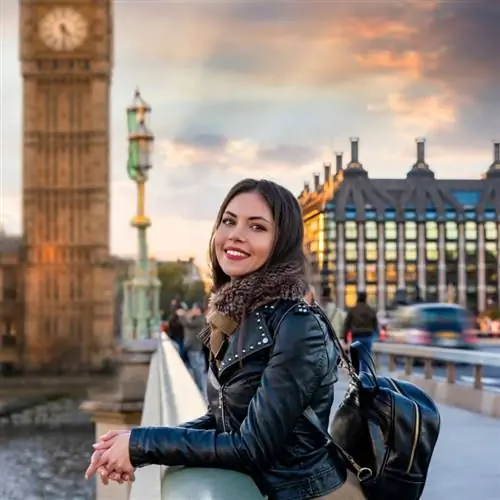 Женщина позирует на мосту в Лондоне, когда за ее спиной садится солнце