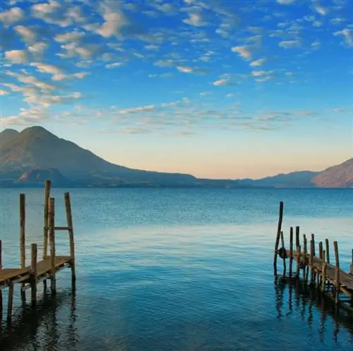 Озеро Атитлан в Гватемале с двумя пирсами, выходящими в воду, и двумя горами вдали.