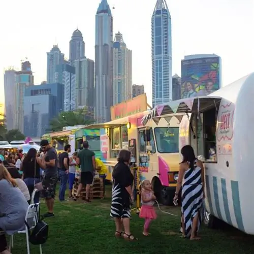 Дубай, ОАЭ Люди отдыхают возле фургонов с едой на Food Truck Jam, мероприятии выходного дня с фургонами с едой и живой музыкой в гольф-клубе Emirates. Дубай Медиа Сити на заднем плане.