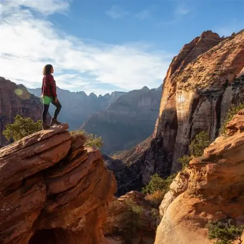 Девушка стоит на красной скале в окружении других скалистых вершин в национальном парке Зайон.