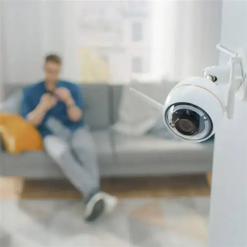 Крупным планом объектный снимок современной камеры наблюдения Wi-Fi с двумя антеннами на белой стене в уютной квартире.