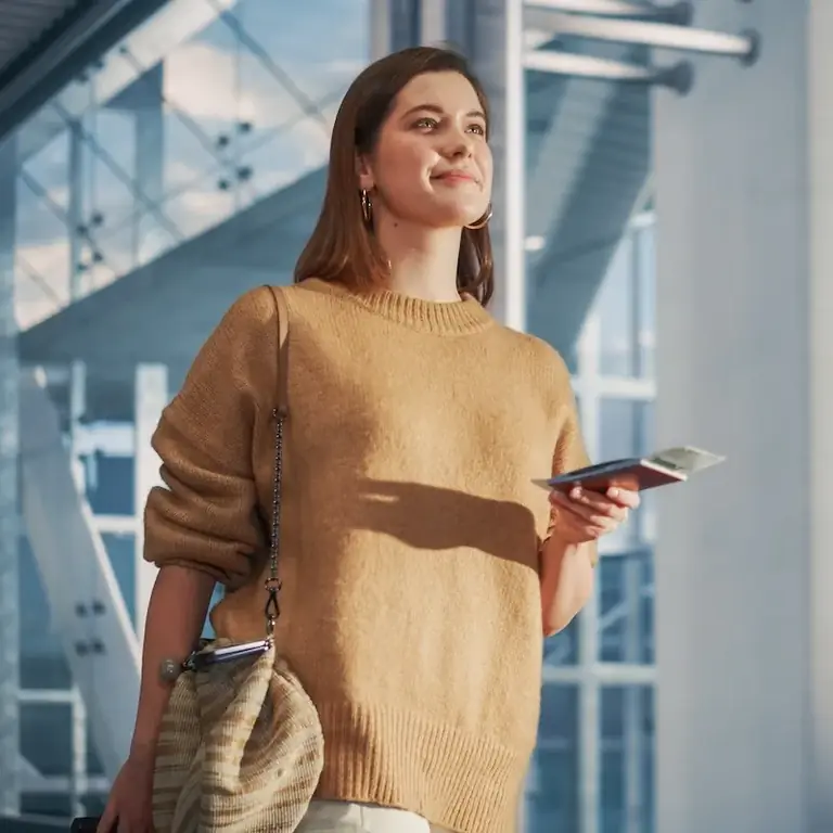 Улыбающаяся женщина идет по аэропорту с паспортом в руке