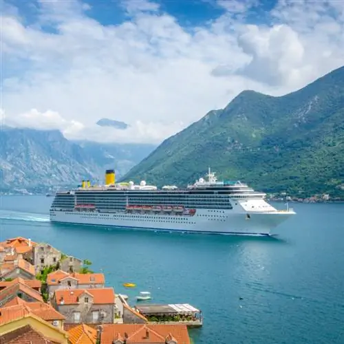 Круизный лайнер, плывущий между высокой горой и маленьким европейским городком