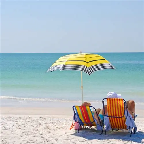 Пара сидит на шезлонгах под зонтиком на пляже.