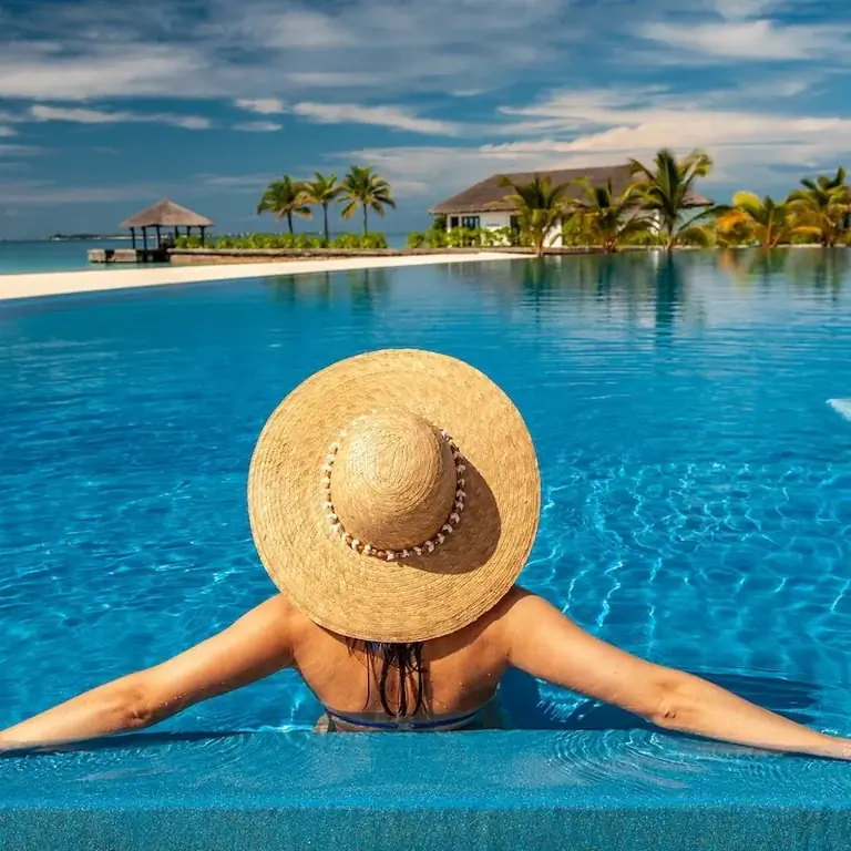Женщина в шляпе расслабляется у бассейна курорта