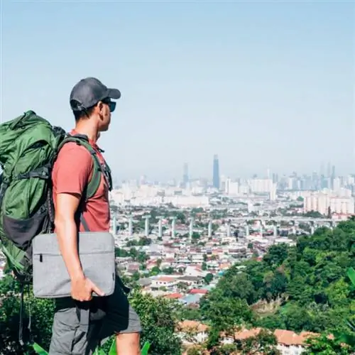 Путешественник держит ноутбук и смотрит на город