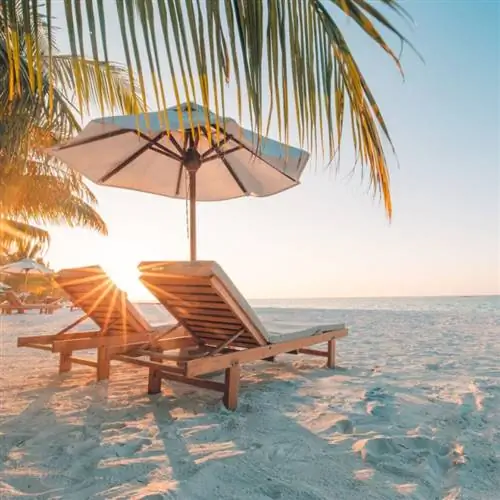 Шезлонги сидят на белом песчаном пляже под зонтиком на закате