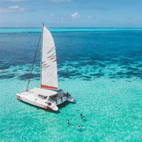 Катамаран плывет по мелководью океана, рядом плавают люди