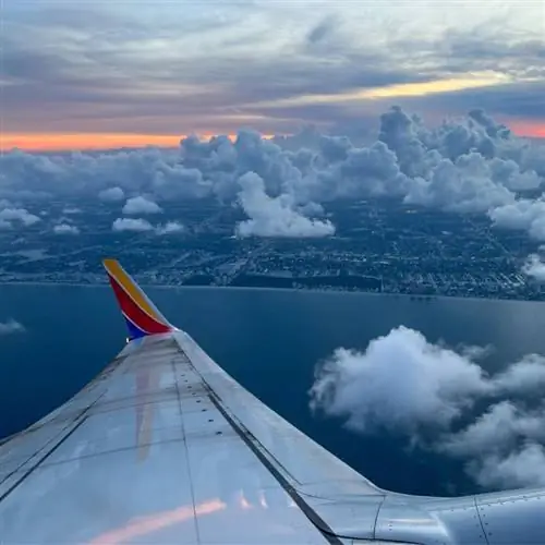 Вид из окна юго-западного рейса на крыло самолета, облака и город вдалеке.