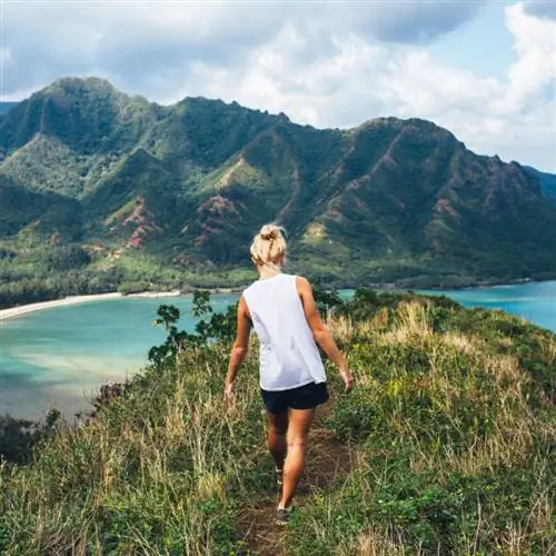 Девушка поднимается на гору с видом на пляж и океан на Гавайях