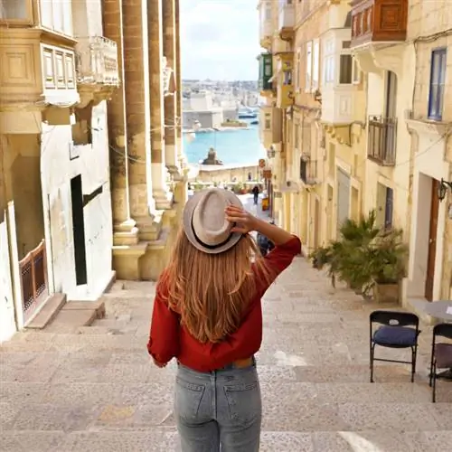 Отдых на Мальте. Вид сзади на женщину-путешественницу, спускающуюся по лестнице в историческом городе Валлетта,